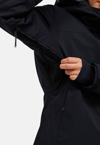 Giubbotto impermeabile blu navy con zip sotto le ascelle, polsini regolabili e tessuto testurizzato con dettagli delle cuciture.