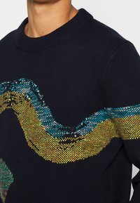 Pull en tricot bleu marine présentant un motif ondulé multicolore en turquoise, jaune et vert sur la poitrine. Design classique à col rond.