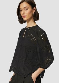 Zwarte blouse met decoratieve uitsnijdingen, een ronde halslijn met een sleutelgat en pofmouwen. Eindigt met een gegolfde zoom.