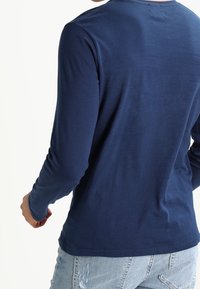 Marinblå långärmad skjorta med rundad hals, tillverkad av ett glatt tyg, med en figurnära design och diskreta sömnadsdetaljer på baksidan.