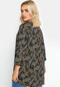 Czarna bluzka z wielokolorowym wzorem w kropki w odcieniach pomarańczowym, zielonym i białym. Ubranie ma rękawy o długości siedmiu ósmych i luźny krój.