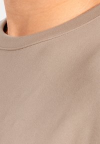 Beige Kurzarmhemd mit einer glatten, weichen Textur und einem Rundhalsausschnitt. Diese Nahaufnahme zeigt die Stoffdetails ohne sichtbare Nähte.