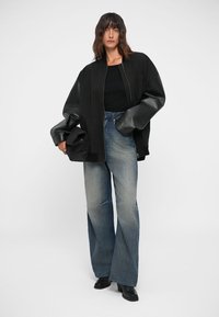 Oversized black bomber jacket with leather sleeves, paired with light blue wide-leg jeans featuring distressed details and black ankle boots.