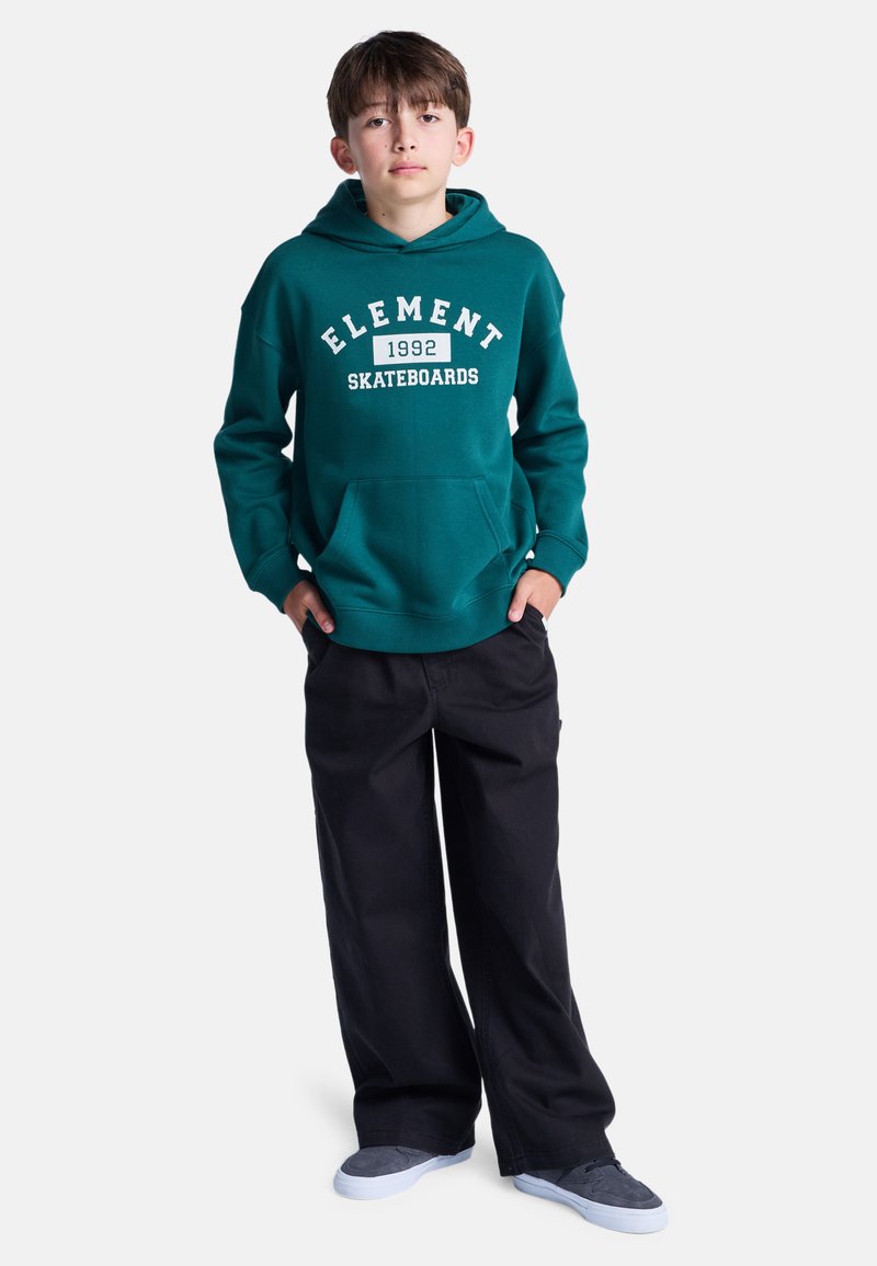 Sudadera verde con impresión "ELEMENT 1992 SKATEBOARDS", bolsillo frontal, combinada con pantalones amplios negros y zapatillas grises.