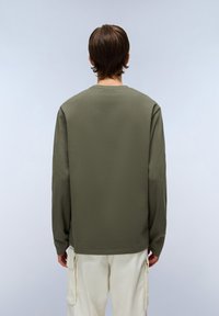 Camicia a maniche lunghe verde oliva realizzata in tessuto morbido, con scollo tondo e vestibilità comoda, abbinata a pantaloni cargo chiari.