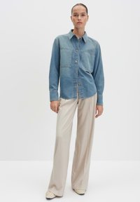 Camicia di denim classica di colore azzurro chiaro, con due tasche frontali, stile con bottoni e vestibilità comoda, abbinata a pantaloni beige a gamba larga.