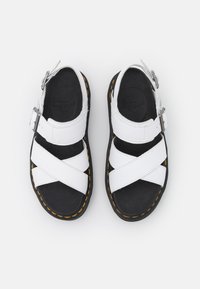 Weiße Ledersandalen mit überkreuzten Riemen, schwarzem gepolstertem Fußbett, schwarzer Außensohle und gelben Nähdetails. Verstellbare Schnallenverschluss.