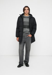 Giubbotto imbottito nero con cappuccio, maglione a righe grigie e nere con texture, jeans grigi e sneakers nere. Design minimalista senza loghi visibili.