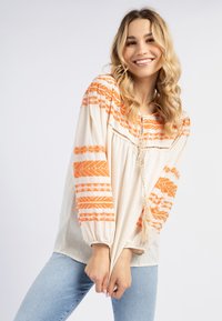 Bohemisk stil bluse i beige stof med orange geometriske mønstre, der har ballonærmer, en blondes neckline og en dekorativ kvast.