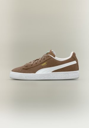 Baskets Puma en daim marron avec semelle blanche et bande latérale blanche, vues de côté sur un fond uni neutre.