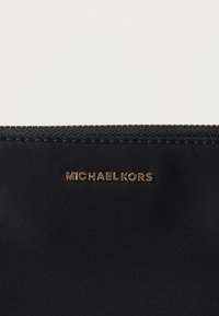 Crni platneni novčanik sa zlatnim logotipom "MICHAEL KORS", ima zatvarač na patent i glatku teksturu. Jednostavan dizajn s minimalnim detaljima.