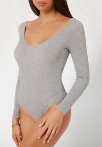 Body grigio a maniche lunghe realizzato in tessuto a coste, con scollatura a V profonda e gambe alte, caratterizzato da una texture liscia e un design aderente.