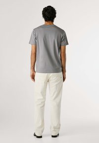 T-shirt grigio a maniche corte con collo a giro, abbinato a pantaloni di colore chiaro. Il tessuto appare liscio e leggero. Visuale dal retro.