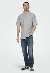 Korte mouwen, lichtgrijze overhemden met knopen, een zak en kraag, gecombineerd met donkerblauwe jeans en zwarte sneakers met witte zolen.