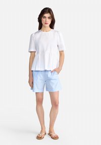 Hvid peplum-top med korte ærmer og rund hals, parret med lyseblå shorts med opkrøllede kanter og flade beige sandaler.