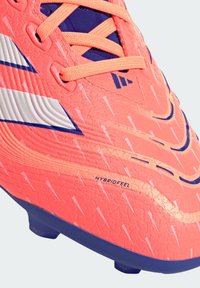 Scarpina da calcio corallo brillante con parte superiore texturizzata, dettagli blu navy e strisce bianche. Presenta il marchio HYBRIDFEEL e lacci arancioni.