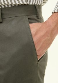 Olivengrüne, leichte Stoffhose mit geradem Schnitt und sichtbarem Seitentasche; glatte Textur und dezente Steppdetails.