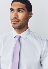 White dress shirt with a smooth texture and a point collar, paired with a solid lavender tie featuring a subtle texture.