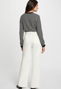 Chemise à manches longues à motif noir et blanc associée à un pantalon large blanc taille haute, présentant une texture lisse et des détails arrière minimalistes.