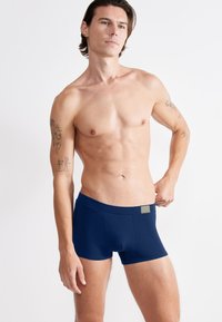 Dunkelblaue Herren-Boxershorts aus weichem Stoff mit glatter Textur und einem breiten elastischen Bund, der mit einem kleinen Logo-Akzent versehen ist.