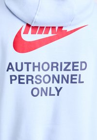 Šviesiai mėlynas džemperis su dideliu raudonu Nike logotipu ir tamsiai pilku užrašu "TIK ĮGALIOTI ASMENYS". Minkšta medžiaga, komfortiškas dizainas.