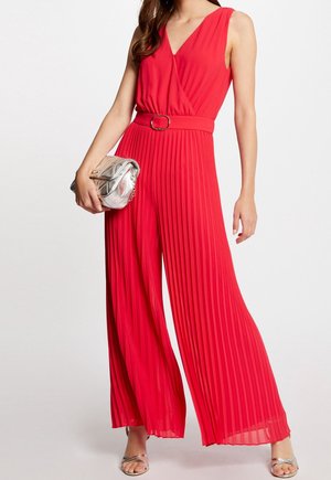 Czerwony kombinezon bez rękawów z dekoltem w serek, plisowanym wzorem i paskiem w talii. Dobrany do niego srebrna pikowana kopertówka i błyszczące sandały.