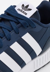 Tumedat sinised Adidas sneakerid, millel on valged kolm triipu, tekstureeritud kanga ja sünteetilised materjalid, pehmendatud keelega ja kummitald.