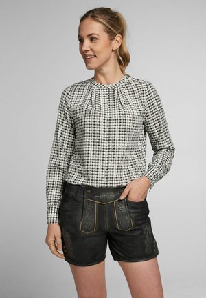 Schwarz-weiß karierte Bluse mit plissiertem Kragen, kombiniert mit schwarzen Ledershorts mit dekorativen Akzenten und sichtbaren Nähten.
