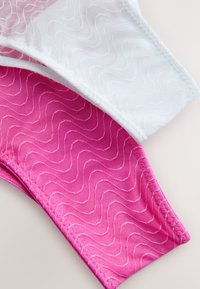 Close-up of pink and white fabric with wavy stitched patterns and zigzag seam edges on a light background.