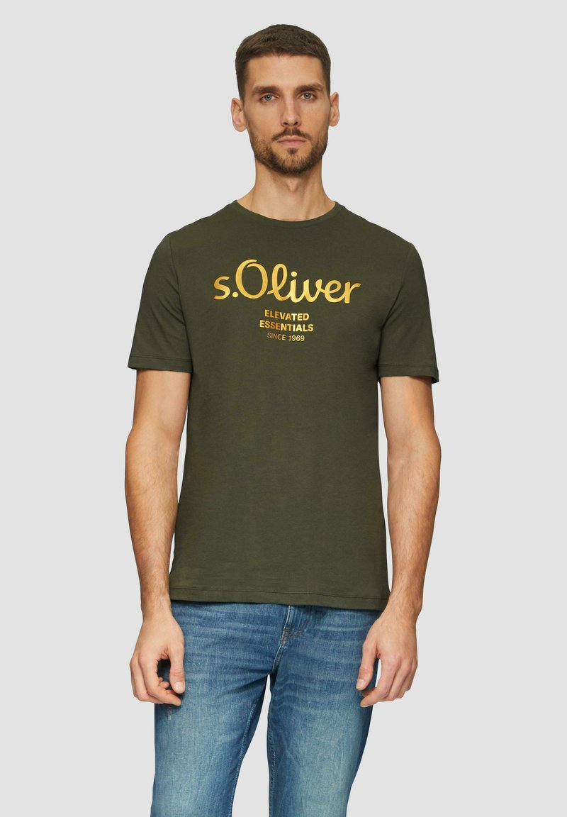 Olive roheline puuvillane T-särk lühikeste varrukatega, ümar kaelus ja kollane trükitud tekst "s.Oliver Elevated Essentials Since 1969."