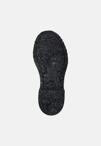 Suela de zapato de goma negra con patrón de agarre texturizado, que presenta un detalle de logotipo en relieve en el centro y un diseño de punta redondeada.