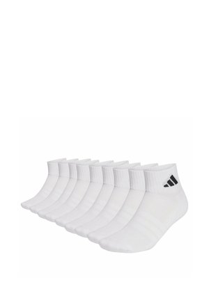 Dix paires de chaussettes blanches aux chevilles avec le logo Adidas noir empilées en rang sur un fond blanc.