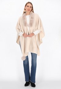 Poncho bej cu un guler din blană artificială și un accent cu pompon. Fabricat dintr-un material moale, având un design lejer și două buzunare frontale.
