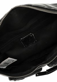 Wnętrze czarnej skórzanej torebki o gładkiej fakturze, z zamykaną na zamek kieszenią i płaską metką. Główna komora jest wyściełana ciemną tkaniną.