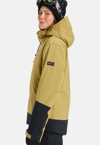 Gelb-schwarze Winterjacke mit Kapuze, ausgestattet mit einem Logo am Ärmel, verstellbaren Kordeln und robuster Stoffstruktur.