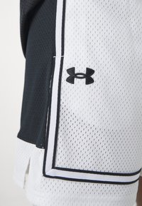 Black and white mesh sports shorts with side slits, featuring a black Under Armour logo and contrasting stitching along the seams.