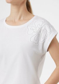 Weißes Baumwoll-T-Shirt mit rundem Ausschnitt und kurzen Ärmeln. Verfügt über ein detailliertes graues gesticktes Blumenmotiv auf der linken Schulter.