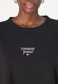 Black sweatshirt featuring a ribbed crew neckline and 'tommy jeans' logo in white, with a small red, white, and blue flag accent underneath.