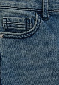 Tessuto di denim in azzurro chiaro, con una piccola tasca frontale con dettagli cuciti e un bottone metallico visibile con logo in rilievo.