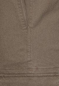 Bruine katoenen stof met een gladde textuur, met gedetailleerde stiksels en een verticale naad, typisch voor casual broeken.