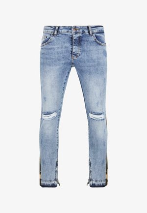 Heledad sinise värviga teksapüksid, millel on kulumise detailid, rebenenud kohad põlvede juures ja tõmblukkudega aktsendid välistel õmblustel. Kitsas lõige.