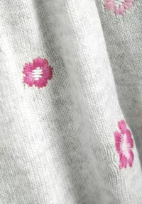 Grijze gebreide stof met roze geborduurde bloemen en witte accenten, die een zachte textuur en een gedetailleerd bloemenpatroon laat zien.
