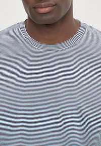 Camiseta de rayas con finas franjas azul marino y blancas, escote redondo y textura suave. Costuras visibles alrededor del cuello.