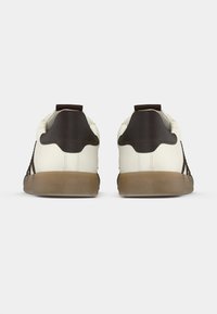 Valged tossud pruunide detailidega; sile pealmine materjal, tekstuuriga kand ja kummist talla. Omavad minimalistlikku disaini peene viimistlusega.