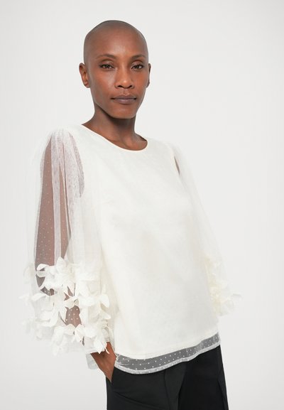 Bela bluzica s prozirnimi rukavima s točkicama, koja ima cvjetne naglaske na manžetama i �čvrsto tijelo s zaobljenim izrezom.