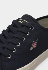 Μπλε ναυτικό πάνινο παπούτσι με μαύρα κορδόνια, μεταλλικά γαντζάκια, λευκή σόλα και κεντημένο λογότυπο GANT με ασπίδα στο πλάι.