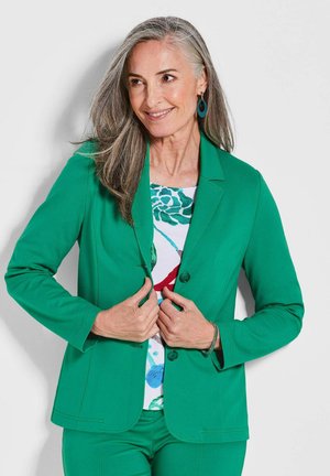 Blazer vert à coupe ajustée, fermeture à un bouton, col cranté et manches longues. Porté au-dessus d'un haut à motif floral.