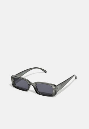 Gafas de sol rectangulares con un marco translúcido de color gris oscuro, lentes oscuros y patillas delgadas. Detalle de logotipo destacado en el marco.