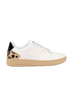 Zapatilla blanca de caña baja con suela beige, parche en el talón con estampado de leopardo, lengüeta negra en el talón y cordones blancos sobre un fondo blanco liso.