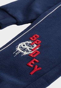 Námořnické modré tepláky vyrobené z měkké látky s bílým vzorem pavučiny a červeným vyšívaným textem "SPYDER" podél nohy.